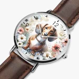 May include: A silver wristwatch with a brown leather band. The watch face features a watercolor illustration of a dachshund dog surrounded by flowers in shades of pink, white, and blue. The watch has black numerals.
