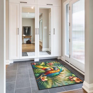 May include: A rectangular doormat with a colourful illustration of two macaws amidst green foliage and pink flowers. The macaws have blue, yellow, orange, and green feathers. The mat is on a grey tiled floor, near a white door.