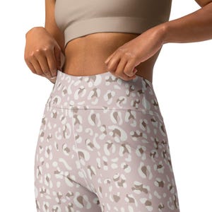 Op de afbeelding: Hoge taille leggings met een lichtroze achtergrond en een patroon van witte en bruine dierenprint vlekken. De leggings zijn gemaakt van een rekbaar materiaal en zijn ontworpen voor sportieve activiteiten.