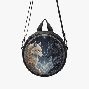 May include: A circular black crossbody bag with an illustration of two wolves. One is white with gold detailing, the other black. The background shows a starry night sky and clouds. The bag has a handle and a shoulder strap.