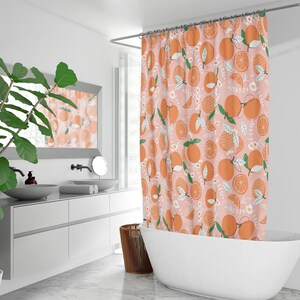 Pu&ograve; includere: Una tenda da doccia rosa con un motivo ripetitivo di fette d'arancia e foglie verdi. La tenda da doccia &egrave; appesa in un bagno con una vasca da bagno bianca e un mobile da bagno bianco.