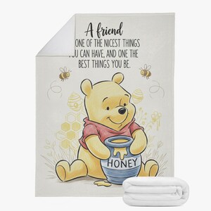 May include: A soft, white blanket featuring a cartoon illustration of Winnie the Pooh holding a honey pot. The blanket has the text "A friend, one of the nicest things you can have, and one the best things you be."