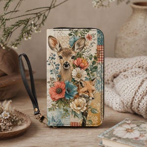 Puede incluir: Cartera con cremallera con un diseño de ciervo y zorro rodeados de flores coloridas. El diseño incluye flores rojas, azules y crema, sobre un fondo de retazos. Una correa de muñeca negra está unida a la cartera.