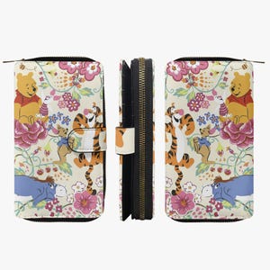 May include: A beige wallet featuring a floral pattern with Winnie the Pooh characters. The design includes Pooh Bear, Tigger, Piglet, and Eeyore amidst pink flowers and green vines. The wallet has a zipper closure and a snap closure.