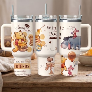 Peut inclure: Trois gobelets isothermes blancs avec poignées, chacun orné d'illustrations de Winnie l'Ourson. L'un montre Winnie avec du miel, un autre avec une cuillère à miel, et le troisième avec Winnie et Porcinet. Le texte comprend "Sweet Cake", "Winnie the Pooh", et "Hunny love".