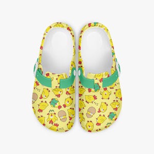 May include: A pair of yellow clogs with a repeating pattern of cartoon chicks in various poses. The clogs have green straps and white inner soles. The overall design is playful and suitable for casual wear.