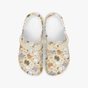 May include: A pair of beige clogs with a repeating pattern of cartoon chickens in various colors. The clogs have a white interior and a beige strap and button closure. The chickens are in shades of brown, blue, white, and black.