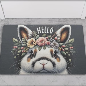 May include: A gray doormat with a white bunny wearing a flower crown. The bunny is looking at the camera and the text "HELLO" is above the bunny.