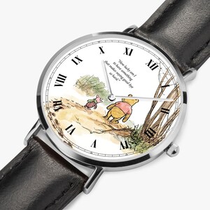 Pode incluir: Rel&oacute;gio de pulso prateado com bracelete em couro preto. O mostrador apresenta uma ilustra&ccedil;&atilde;o em aquarela de Winnie the Pooh e Piglet, algarismos romanos e a cita&ccedil;&atilde;o: "How lucky am I to have something that makes saying good-bye so hard."