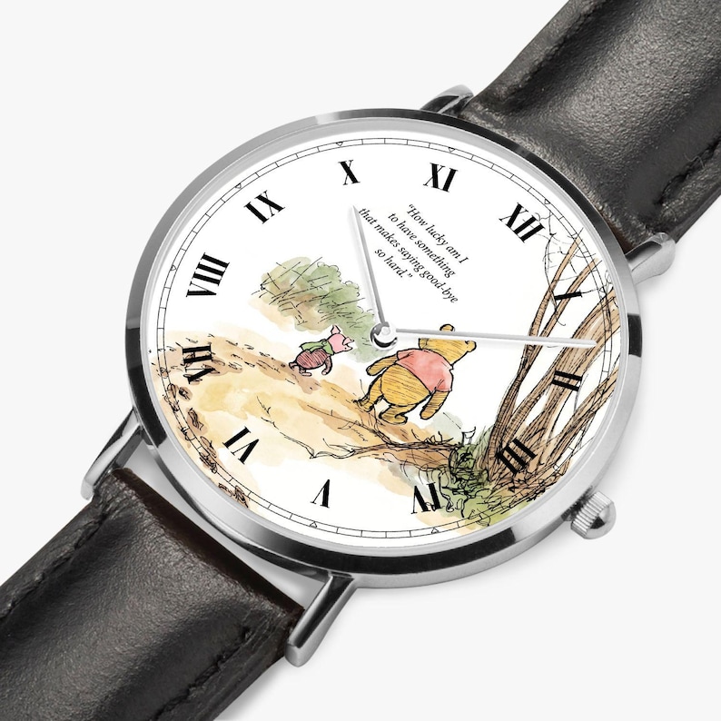 Pode incluir: Rel&oacute;gio de pulso prateado com bracelete em couro preto. O mostrador apresenta uma ilustra&ccedil;&atilde;o em aquarela de Winnie the Pooh e Piglet, algarismos romanos e a cita&ccedil;&atilde;o: "How lucky am I to have something that makes saying good-bye so hard."