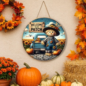 Peut inclure: Panneau rond en bois avec une scène d'automne peinte. Il présente un épouvantail, un camion bleu, des citrouilles et des tournesols. Le panneau indique "WELCOME TO MY PATCH" et est orné d'une couronne d'automne et de citrouilles.
