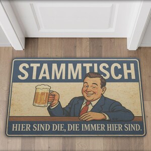 May include: Rectangular doormat with a vintage design. The mat features a smiling man holding a beer mug, with the German text "STAMMTISCH" and "HIER SIND DIE, DIE IMMER HIER SIND." in a blue and beige color scheme.
