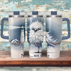 May include: Three stainless steel tumblers with lids and handles. The tumblers feature different designs. One has a lighthouse, another has a white bird with a blue background, and the third has a white bird with a blue background and the text "No... not today".