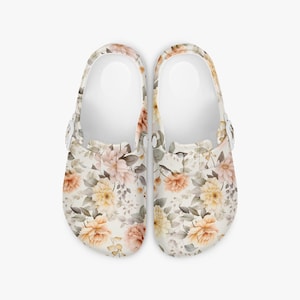May include: Pair of white clogs with a floral pattern featuring peach, yellow, and pink flowers with green leaves. The clogs have a strap and a white interior.
