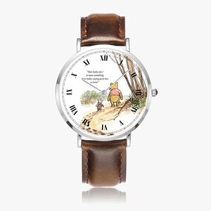 Pode incluir: Um rel&oacute;gio de pulso com pulseira de couro castanho e mostrador branco. O mostrador apresenta uma ilustra&ccedil;&atilde;o em aquarela de Winnie the Pooh e Piglet caminhando em um caminho, com a cita&ccedil;&atilde;o "How lucky am I to have something that makes saying good-bye so hard."