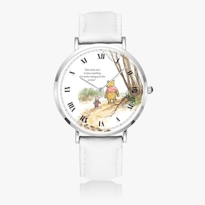 Pode incluir: Um rel&oacute;gio de pulso com pulseira de couro branco e caixa prateada. O mostrador do rel&oacute;gio apresenta uma ilustra&ccedil;&atilde;o em aquarela de Winnie the Pooh e Piglet caminhando em um caminho, com a cita&ccedil;&atilde;o "How lucky am I to have something that makes saying good-bye so hard."