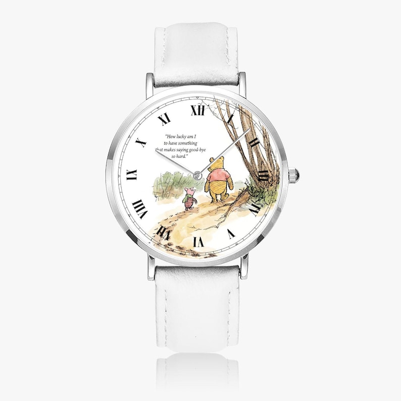 Pode incluir: Um rel&oacute;gio de pulso com pulseira de couro branco e caixa prateada. O mostrador do rel&oacute;gio apresenta uma ilustra&ccedil;&atilde;o em aquarela de Winnie the Pooh e Piglet caminhando em um caminho, com a cita&ccedil;&atilde;o "How lucky am I to have something that makes saying good-bye so hard."