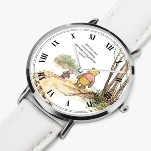 Pode incluir: Um rel&oacute;gio de pulso prateado com uma pulseira de couro branca. O mostrador do rel&oacute;gio apresenta uma ilustra&ccedil;&atilde;o em aquarela de Winnie the Pooh e Piglet, com algarismos romanos e a cita&ccedil;&atilde;o: "How lucky am I to have something that makes saying good-bye so hard."