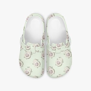 May include: A pair of light green clogs with a repeating pattern of avocado-shaped figures, each with a heart-shaped pit. The clogs have white interiors and adjustable straps. The word "Love" is printed on the side of the clogs.