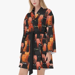 May include: A black robe with a repeating pattern of orange and red cat illustrations. The robe has a black belt and white trim on the sleeves. The cat illustrations have black eyes and are interspersed with leaf designs.
