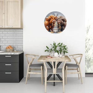May include: A round wall clock with a white face and black Roman numeral hour markers. The clock features a colourful illustration of two Highland cows eating noodles from a bowl. The clock is hanging on a white wall in a kitchen setting.