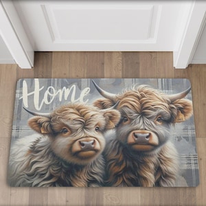 以下が含まれることがあります： 「Home」と印刷されたドアマット。茶色と白の毛並みのハイランド牛が2頭、ドアマットに描かれています。牛は格子柄の背景になっています。