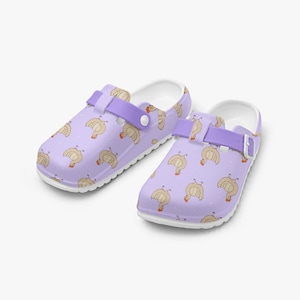 May include: A pair of lavender clogs with a white sole and a lavender strap. The clogs are decorated with a pattern of cartoon chickens and white polka dots. The strap has a white button and a metal buckle.