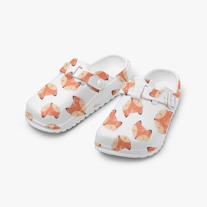 May include: White clogs with a repeating pattern of orange and tan foxes. The clogs have a strap that can be adjusted. The shoes are made of a smooth, glossy material.