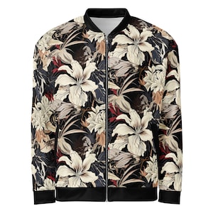Puede incluir: Una chaqueta bomber negra con estampado floral con flores blancas, beige y rojas. La chaqueta tiene cierre de cremallera y puños y dobladillo de canalé.