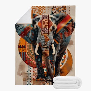 Può includere: Una coperta decorativa con una dettagliata illustrazione di un elefante adornato con motivi tribali nei toni dell'arancione, del rosso, del blu e del marrone. L'elefante ha grandi zanne ed è ambientato su uno sfondo beige. Una coperta bianca piegata è in basso.