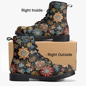 Könnte beinhalten: Schwarze Combat-Stiefel mit einem farbenfrohen Blumenmuster. Die Stiefel haben eine Schnürung und eine robuste schwarze Sohle. Das Blumenmuster umfasst rote, gelbe, blaue und grüne Blumen und Blätter. Die Stiefel werden auf einem Karton präsentiert.
