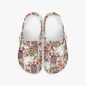 Könnte beinhalten: Cremefarbene Clogs mit einem verspielten Muster. Das Muster zeigt braune Teetassen, rote Pilze, Erdbeeren und weiße Wolken. Die Clogs haben ein weißes Innenfutter und einen verstellbaren Riemen.