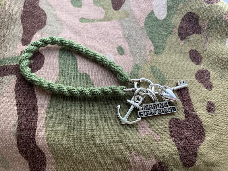 May include: A green braided cord keychain with a silver anchor charm, a silver heart charm, a silver key charm, and a silver charm with the text "MARINE GIRLFRIEND".