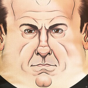 May include: A close-up illustration of a face with a stern expression. The image features a light skin tone, brown eyes, and dark eyebrows. The artwork has visible lines and wrinkles, suggesting an older age. The background is a neutral beige color.