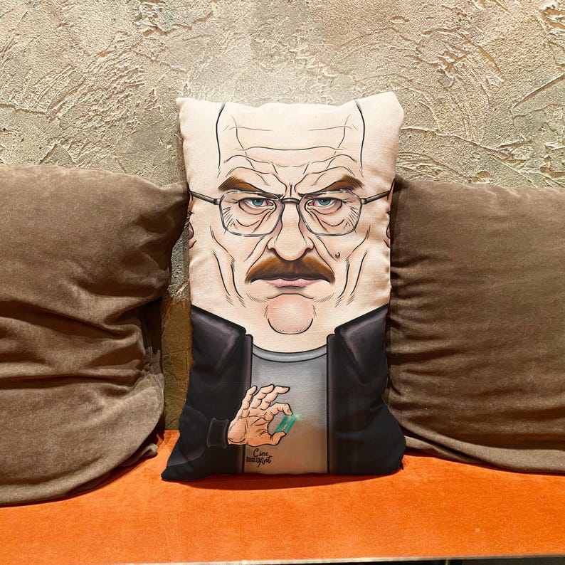 Op de afbeelding: Een decoratief kussen met een cartoonillustratie van Walter White uit de tv-serie Breaking Bad. Het kussen is wit met een zwarte achtergrond en toont Walter White die een blauwe kristal in zijn hand houdt. De tekst "Cine" staat in de rechterbenedenhoek van het kussen.