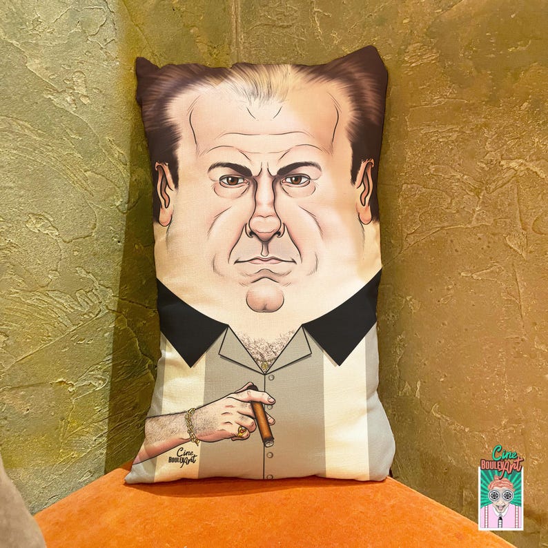 May include: A decorative pillow featuring a stylized illustration of a man with a cigar. The pillow has a light gray and white striped shirt with a black collar. The illustration includes a gold bracelet and ring. The pillow is rectangular.
