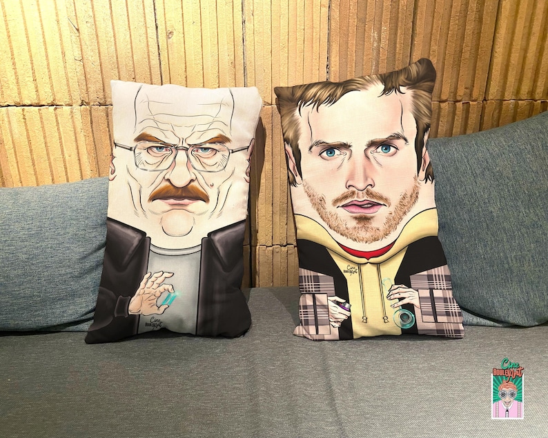 Op de afbeelding: Twee decoratieve kussens met cartoon gezichten van Walter White en Jesse Pinkman uit de tv-serie Breaking Bad. De kussens zijn wit met een zwart-wit geruit patroon.