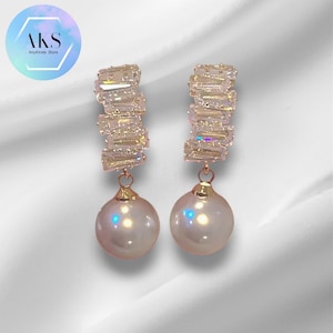 May include: A pair of gold earrings with a pearl drop and a crystal bar design.