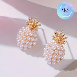May include: A pair of gold pineapple earrings with white pearl accents. The earrings are small and delicate, perfect for adding a touch of whimsy to any outfit.