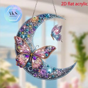 May include: A decorative 2D flat acrylic moon and butterfly hanging ornament. The crescent moon is decorated with colourful gems and a large butterfly. A smaller butterfly hangs below. The ornament is suspended by a chain.