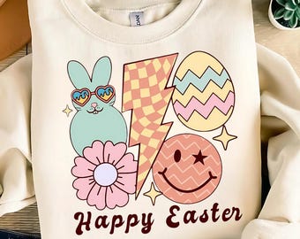 May include: A cream-colored sweatshirt with a graphic design featuring a cartoon bunny wearing heart-shaped sunglasses, a lightning bolt, a smiley face, and an Easter egg. The text "Happy Easter" is printed below the graphic.
