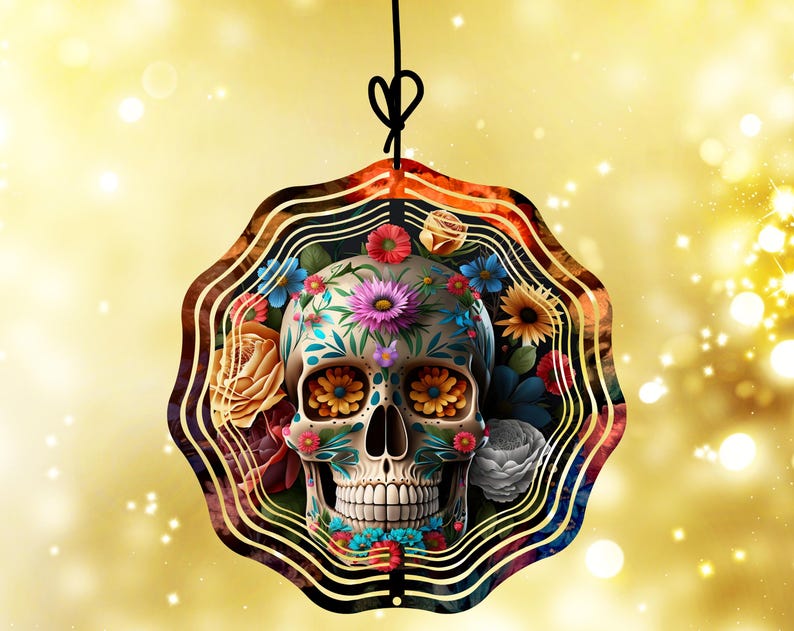 May include: A Day of the Dead-themed ornament featuring a decorated skull with floral accents. The skull is adorned with colorful flowers and intricate patterns, suspended by a black string against a gold background.