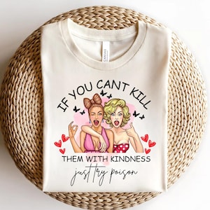 Puede incluir: Camiseta color crema con un gr&aacute;fico de dos mujeres y el texto "IF YOU CAN'T KILL THEM WITH KINDNESS just try poison." Las mujeres visten vestidos rosas y rojos, con mariposas y corazones.