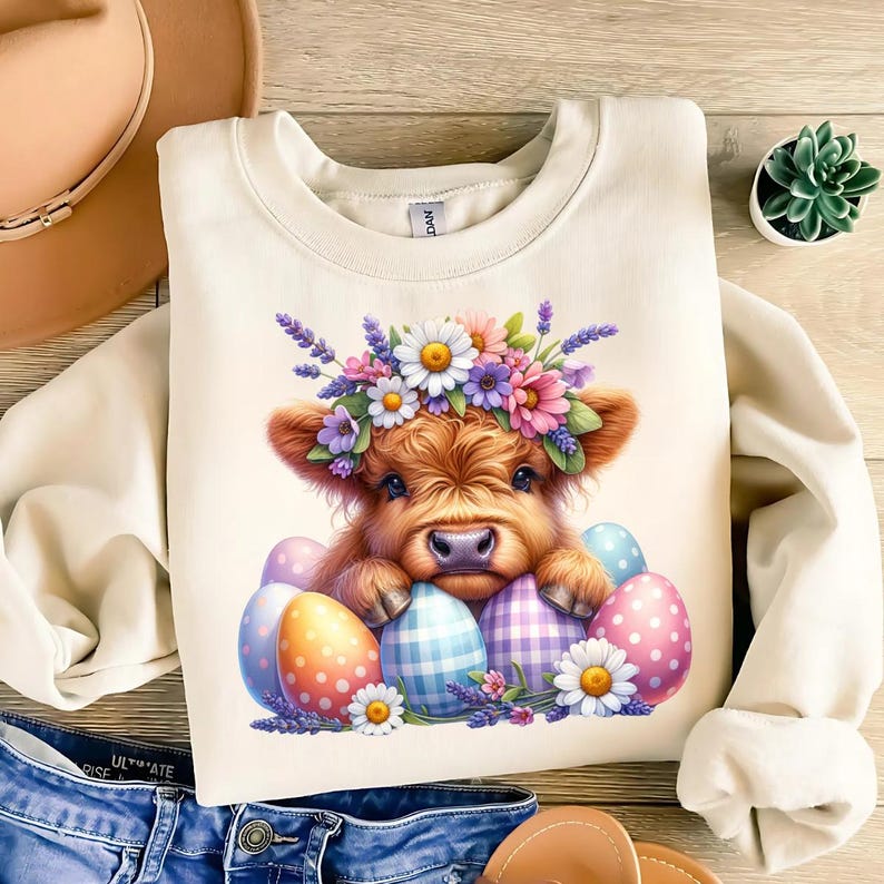 May include: A cream-colored sweatshirt with a cute illustration of a Highland cow wearing a flower crown and surrounded by colorful Easter eggs.