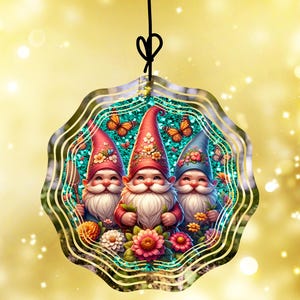 May include: A decorative ornament featuring three smiling gnomes with white beards and red, blue, and pink hats. The gnomes are surrounded by flowers and butterflies, set against a teal background with a gold border. The ornament hangs from a black string.