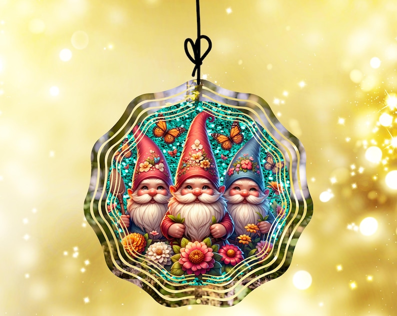 May include: A decorative ornament featuring three smiling gnomes with white beards and red, blue, and pink hats. The gnomes are surrounded by flowers and butterflies, set against a teal background with a gold border. The ornament hangs from a black string.