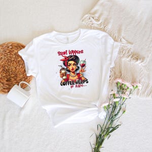 Puede incluir: Camiseta blanca con una ilustraci&oacute;n retro de una mujer sosteniendo caf&eacute; y una copa de vino. El texto de la camiseta dice: "Shit Happens Coffee Helps or Wine..." La mujer de la ilustraci&oacute;n tiene cabello oscuro y lleva una diadema roja.
