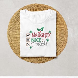 May include: White t-shirt featuring a green holly sprig with red berries. The text reads "Naughty Nice I tried!" with checkmarks and an X next to each word.