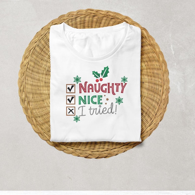 May include: White t-shirt featuring a green holly sprig with red berries. The text reads "Naughty Nice I tried!" with checkmarks and an X next to each word.