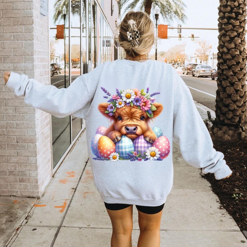 May include: A gray sweatshirt with a graphic of a brown and white Highland cow wearing a flower crown and surrounded by colorful Easter eggs.